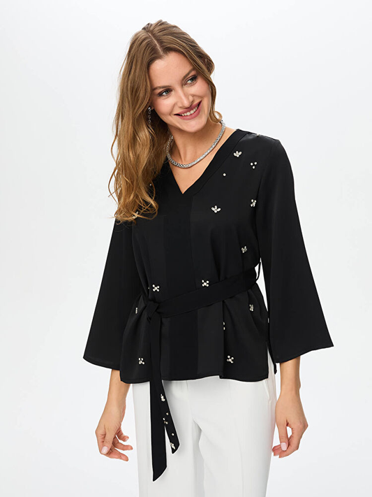 بلوزة من الكريب الساتان بياقة على شكل حرف V مزينة بأحجار وحزام من تصميم فائق سونميز